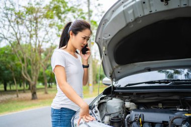 Asian young woman are stressed and calling car insurance. Broken down car while traveling.