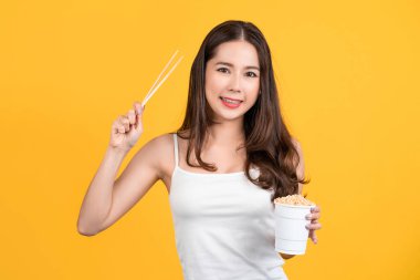Asian young beautiful woman eating hot and spicy instant noodle, beauty face natural makeup, isolated on yellowbackground.