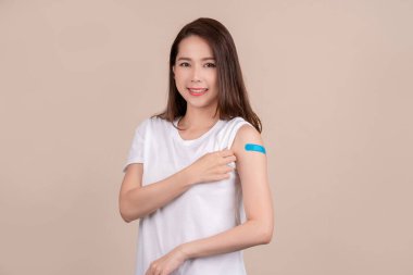 Beautiful asian woman wears adhesive bandage on shoulder recieves vaccine shot isolated over blue background. Successful covid vaccination concept.