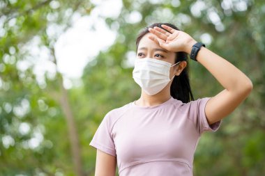 Genç Asyalı fitness sporcusu yoruluyor ve şehrin tozunu ve kirliliğini korumak için maske takıyor.