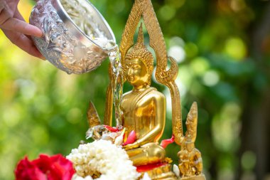 İnsanların elleri Songkran-Tayland 'ın ünlü festivalinde altın Buda heykelinin üzerine su dökmek için metal kase kullanıyor..