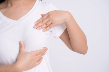 Kadın elleri göğsündeki şişlikleri kontrol ediyor. Gri arka planda göğüs kanseri belirtileri var mı diye. Sağlık sigortası kavramı..