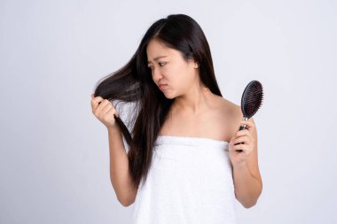 Stresli, Asyalı genç bir kadın beyaz izole edilmiş arka planda ellerinde kuru saçlar tutuyor..