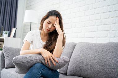 Kanepede oturan mutsuz Asyalı kadın hastalık ve baş ağrısı yüzünden kendini pek iyi hissetmiyordu..