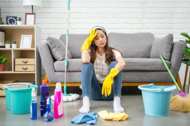 Beautiful Asian housewife feeling tired after doing housework. She sits on the floor in the living room with home cleaning products.