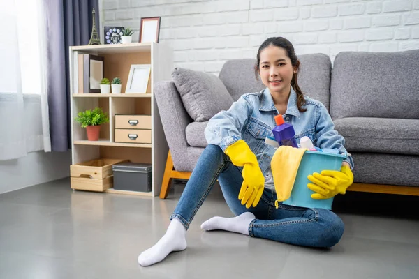 Koruyucu eldivenli güzel bir kadın elinde temizlik için bir şeyler olan kovayla kameraya bakıyor ve evde yerde otururken gülümsüyor..
