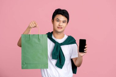 Elinde alışveriş çantaları ve cep telefonu olan yakışıklı Asyalı genç adam, çevrimiçi cep telefonu uygulaması, mal alımı ve teslimatı için boş ekran. 