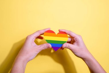 Sarı arka planda kadın eli şeklinde gökkuşağı kalp şeklinde. LGBT, Gurur, LGBTQ Sembolleri