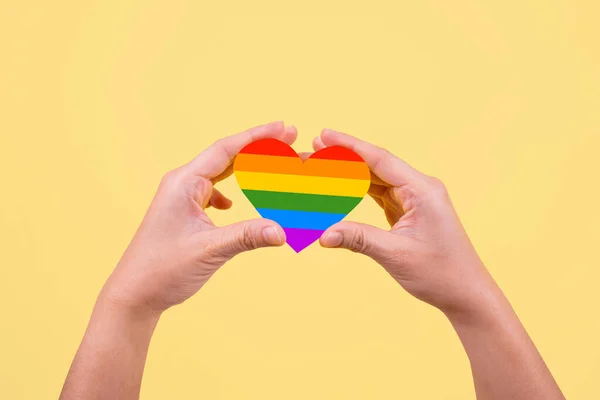 LGBTQ rights concept, Rainbow heart shape in female hand on yellow background.