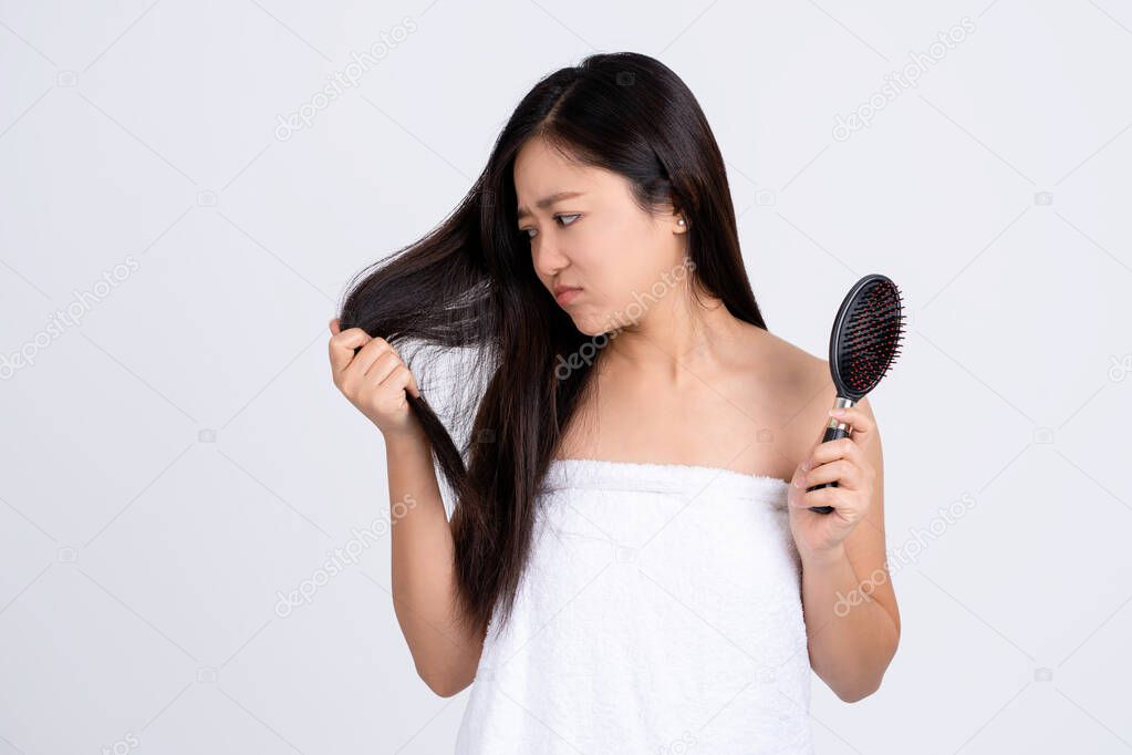Upset stressed young Asian woman holding damaged dry hair on hands over white isolated background.