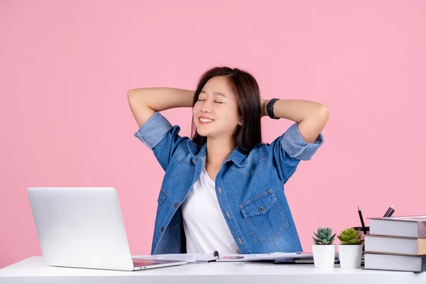 Relaxed Asian businesswoman wearing casual shirt sit work at white office desk isolated on a pink background