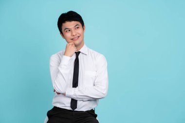 Yakışıklı profesyonel girişimci yeni çalışan ofisini gösteriyor. Açık mavi bir arka planda el çenesine dokunmuş. Düşün, soru ve cevap kavramı.