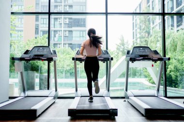 Spor salonundaki koşu bandında koşan Asyalı bir koşucunun arka görüntüsü.