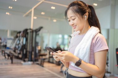 Asyalı güzel kadın spor salonunda akıllı telefon kullanıyor. Egzersiz kavramları.