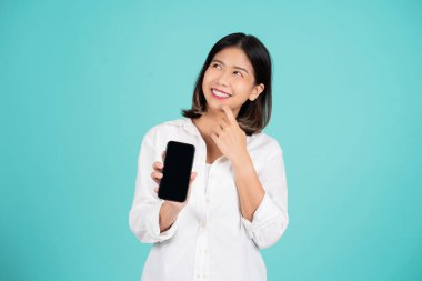 Smiling young asian woman wearing casual clothes standing hold mobile cell phone with blank empty screen mock up copy space isolated on green background.