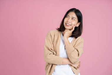 Asian woman thinking something and standing on pink background. Isolated.