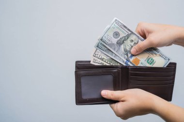 El, gri arka planda izole edilmiş deri cüzdandan dolar çıkardı.
