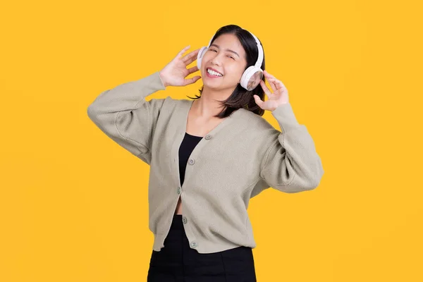 幸せなアジアの美しい女性音楽を聞いて彼女は無線ヘッドフォンを着用し 明るい黄色の背景に隔離された立っています — ストック写真