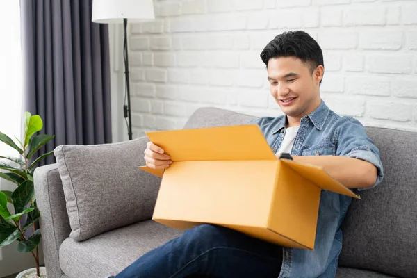 Feliz Joven Asiático Sienta Sofá Desempaca Paquete Casa — Foto de Stock