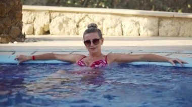 Çekici genç bir kadın jakuzide dinleniyor. Sakin bir atmosferde, rahat bir havuzda dinleniyor..