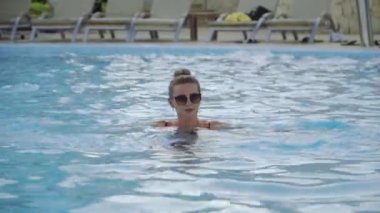 Gülümseyen kadın mavi berrak suyla dolu bir havuzda yüzer. Otelde dinlendirici bir spa 'dan hoşlanıyor..