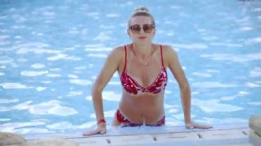 Mayo giymiş, bronz tenli orta yaşlı bir kadın. Mavi su havuzundaki otelde dinleniyor..