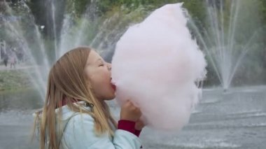 Neşeli, pozitif, okul çağındaki bir kız lunaparkta pamuk şeker yiyor, fıskiyelerin önünde duruyor. Hafta sonu dinlen. Sonbahar.