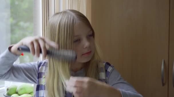 金髪の女子高生が髪の毛を世話している 彼女は櫛で慎重にそれらを磨く — ストック動画
