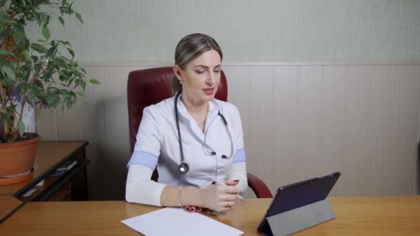 Ofisindeki Masada Oturan Beyaz Önlüklü Dost Canlısı Bir Kadın Doktor — Stok video