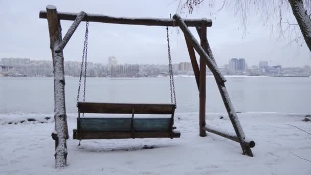 冬には川のそばに白い雪が積もって揺れるベンチ — ストック動画
