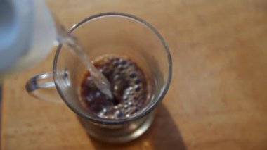 Çaydanlıktan şeffaf bir bardağa sıcak su dökmek. Kahve hazırlığı. Sığ alan derinliği, su jetine odaklan..