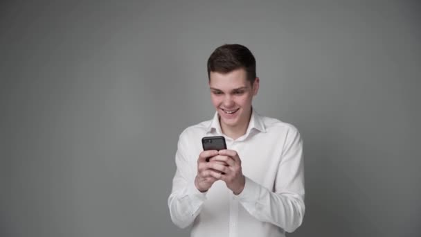 Um cara jovem expressa alegria ao olhar para seu smartphone. — Vídeo de Stock