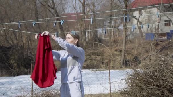 一位年轻的家庭主妇把衣服挂在房子的后院里 妇女的家务劳动 — 图库视频影像
