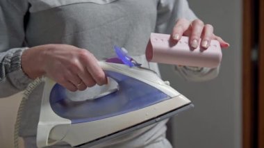 Bir kadın buhar üretmek için demire su döker. Ütü için hazırlanılıyor.