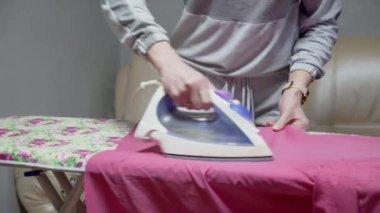 Ev hanımı kadın ütü masasında çarşaf ütülüyor. Rutin ev ödevi.