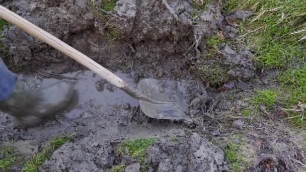 一个穿橡胶靴的人用铲子清理一条水沟 肮脏和繁重的体力劳动 — 图库视频影像