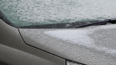 Park halindeki bir arabaya ıslak kar yağıyor. Arabanın karla kaplı yüzeyi ve su damlaları..
