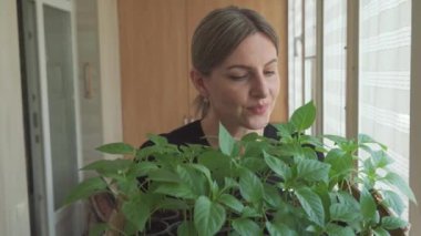 Gülümseyen orta yaşlı kadın evde yetiştirdiği yeşil bitkileri inceliyor. O, evde bahçe işlerini yapmaktan hoşlanır..