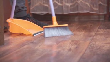 Sweep debris into a dustpan with a long-handled brush. Room cleaning. Lower angle, unrecognizable model.