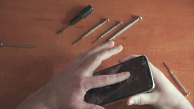 Tamirci kırık camlı akıllı telefonu teftiş ediyor. Telefondaki koruyucu cam çatlaklarla kaplı. Kamera üstte. Akıllı telefon tamir aletleri masanın üstünde..