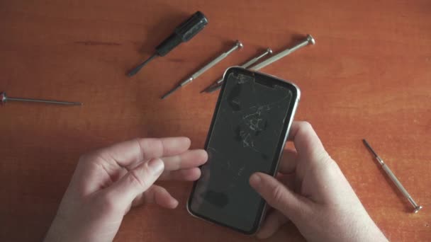 修理工用碎玻璃对智能手机进行了检查 电话机上的防护玻璃上布满了裂缝 摄像头在上面 智能手机的修理工具在桌子上 — 图库视频影像