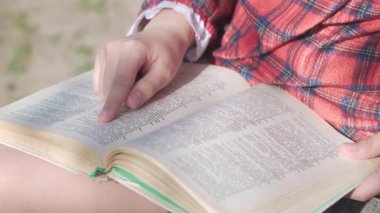 A schoolgirl girl holds a textbook in her hands and reads something carefully. Preparing homework. Close-up, focus on the hands.