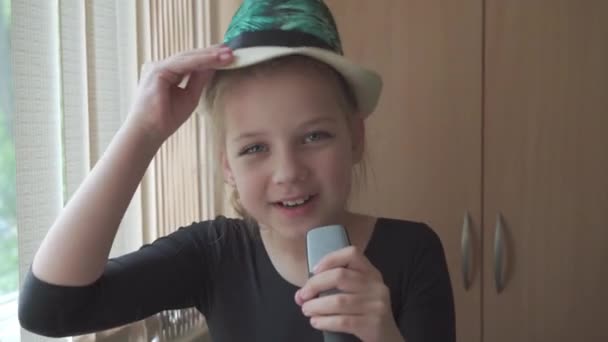 一个快乐的九岁小女孩手里拿着话筒鬼混 她摘下帽子 唱了一首歌 — 图库视频影像
