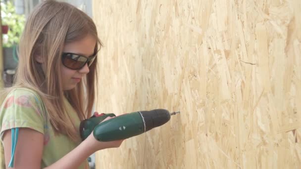 一个戴防护眼镜的年轻女孩学习使用建筑工具工作 她把一个自攻自破的螺丝塞到了木墙上 — 图库视频影像
