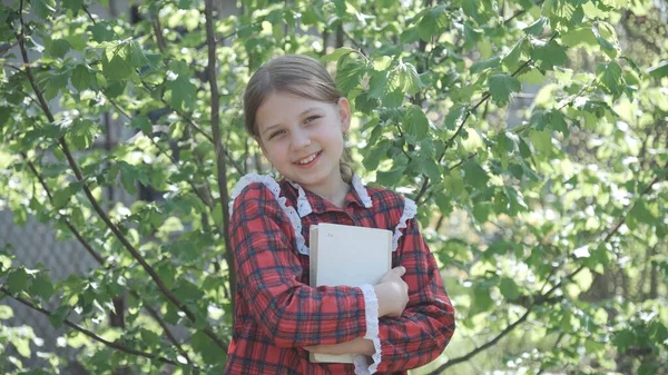 교복을 교과서를 그녀의 얼굴에 미소를 지었어요 그녀는 나무의 배경에 있습니다 — 스톡 사진