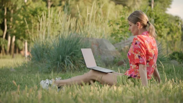 Młoda Kobieta Siedzi Trawie Parku Patrzy Ekran Swojego Laptopa Kształcenie — Zdjęcie stockowe