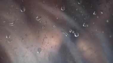 Çamaşır makinesinin içinde, sığ bir alanda çamaşırların taşınması. Cam kapıdaki su damlacıklarına odaklan..