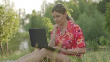 Orta yaşlı bir kadın halka açık bir parkta dizüstü bilgisayarıyla çalışıyor. Yazıyor ve düşünüyor. Yüksek kalite 4k görüntü