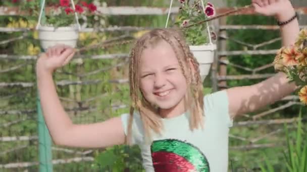 在花园里阳光灿烂的日子里 小女孩高兴地看着摄像机笑了 她用手握住辫子 — 图库视频影像