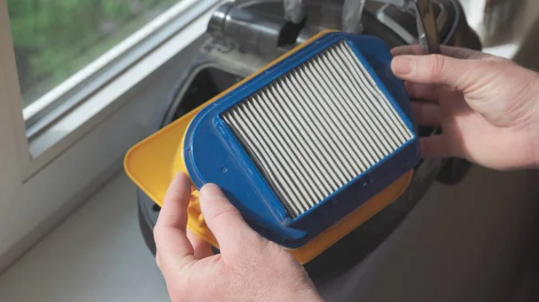 Men's hands remove dirty filter from vacuum cleaner to clean it.